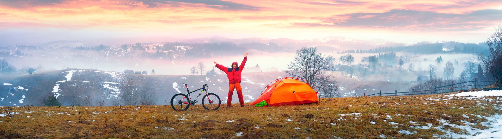 Campeur avec vélo et tente devant un paysage de montagnes et de campagne au petit matin
