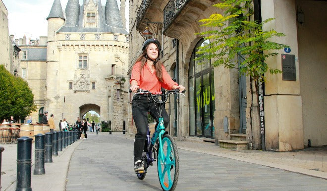 Une jeune femme se rend au travail à l'aide d'un vélo électrique de couleur verte. 