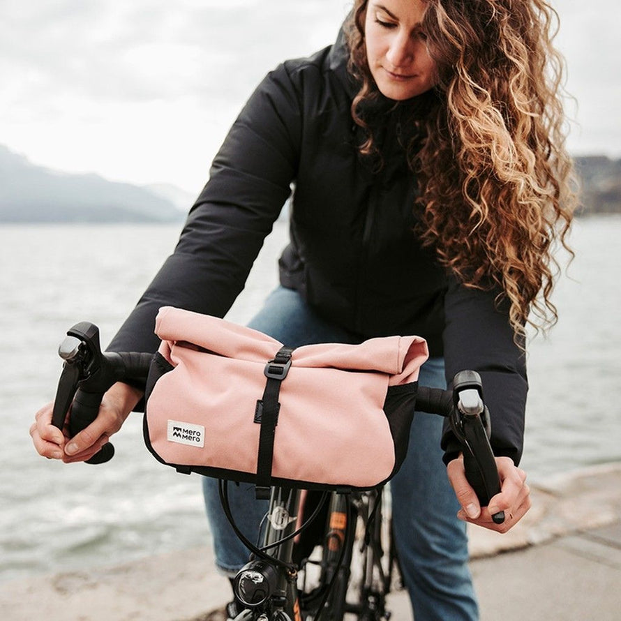 Cycliste roulant avec la sacoche MeroMero Piha rose sur guidon de vélo gravel au bord d’un lac.