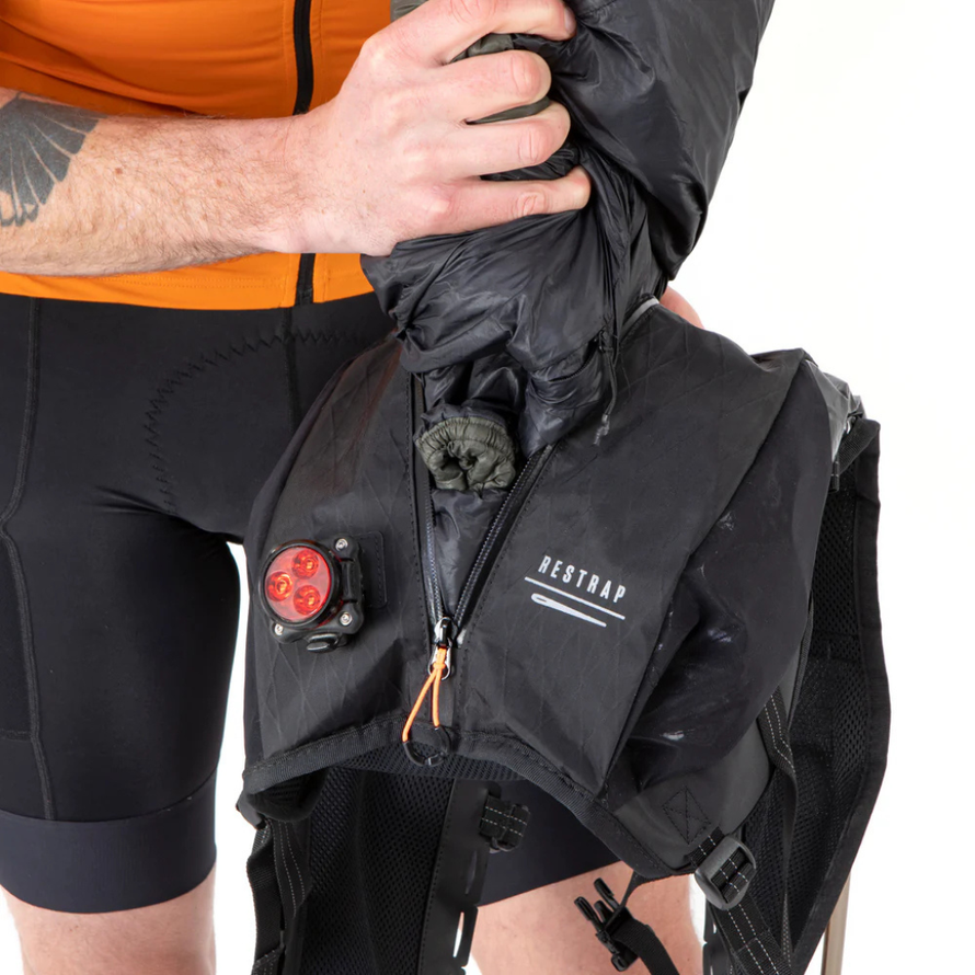 Rangement d’une veste imperméable dans le compartiment arrière de la veste d’hydratation Restrap Race, avec éclairage arrière fixé pour une meilleure visibilité