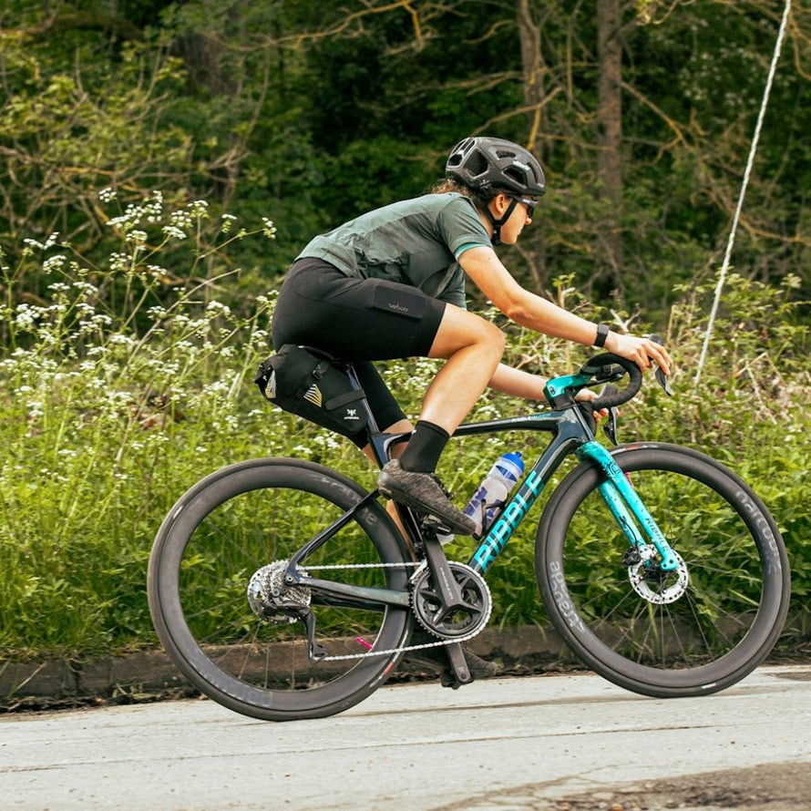 Cycliste avec sacoche de selle bikepacking Apidura Racing noire et jaune sur vélo de route en pleine sortie