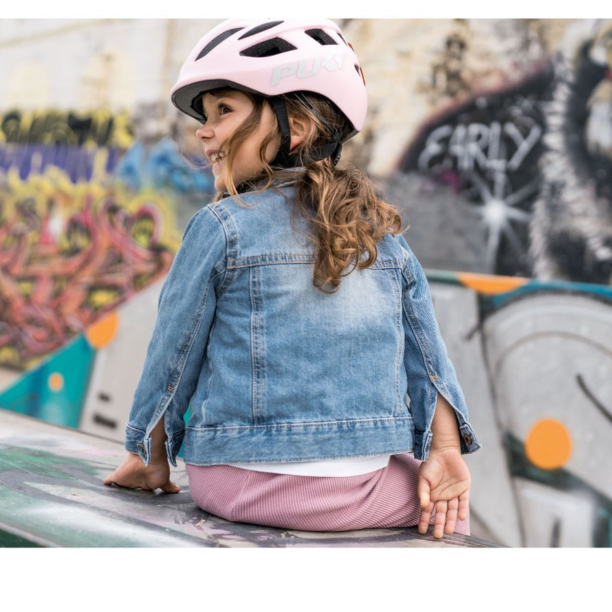 Petite fille portant le casque PUKY rose, assise après une balade à vélo, protégée et détendue