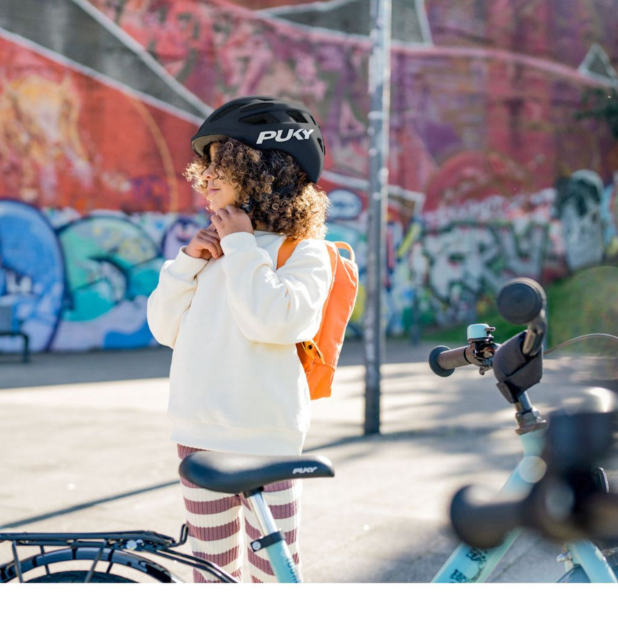 Enfant portant le casque vélo PUKY noir brillant, ajustant la jugulaire avant de partir à vélo en ville