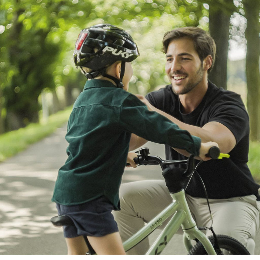 Enfant roulant à vélo avec l'aide d'un adluteavec le casque PUKY noir, protection sûre et design moderne