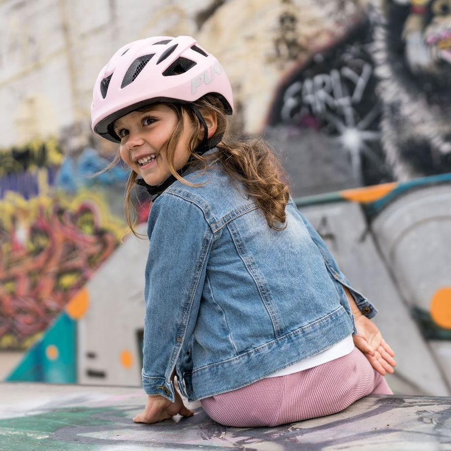 Fille souriante portant le casque vélo PUKY rose rétro, confortablement ajusté pour rouler en toute sécurité