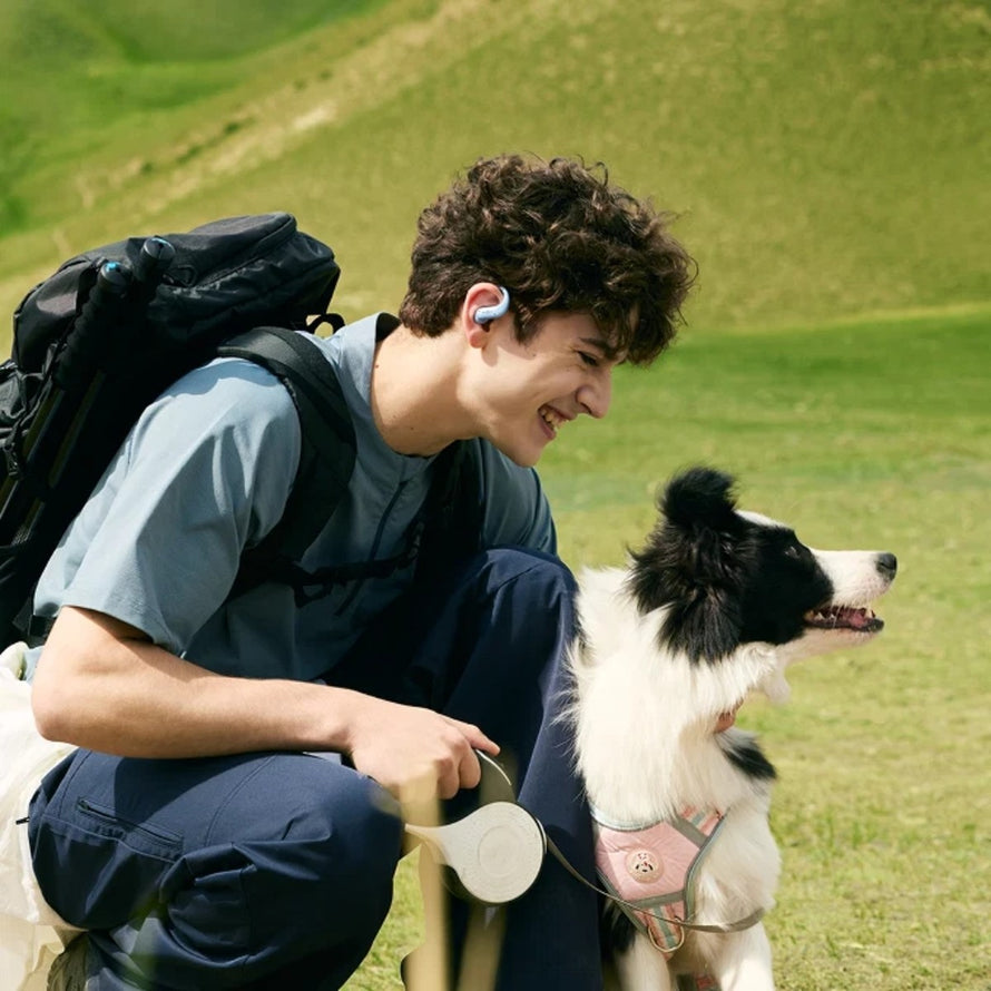Jeune homme avec ecouteurs velo Shokz OpenFit Air 2 profite d'une balade en plein air avec son chien
