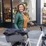 Une femme souriante se tient à côté de son vélo équipé du panier Clipper arrière pour vélo. avec sa housse de transport. 