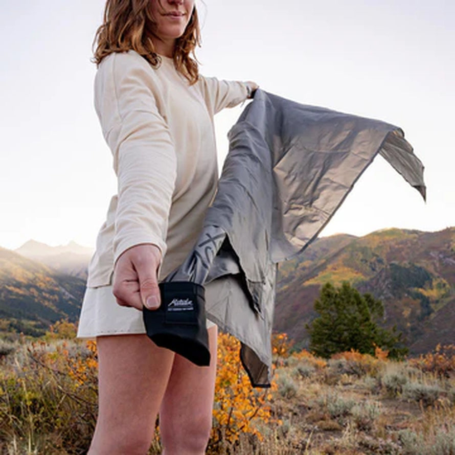 Femme en nature déplie la couverture Matador Pocket Blanket compacte et imperméable pour activités outdoor