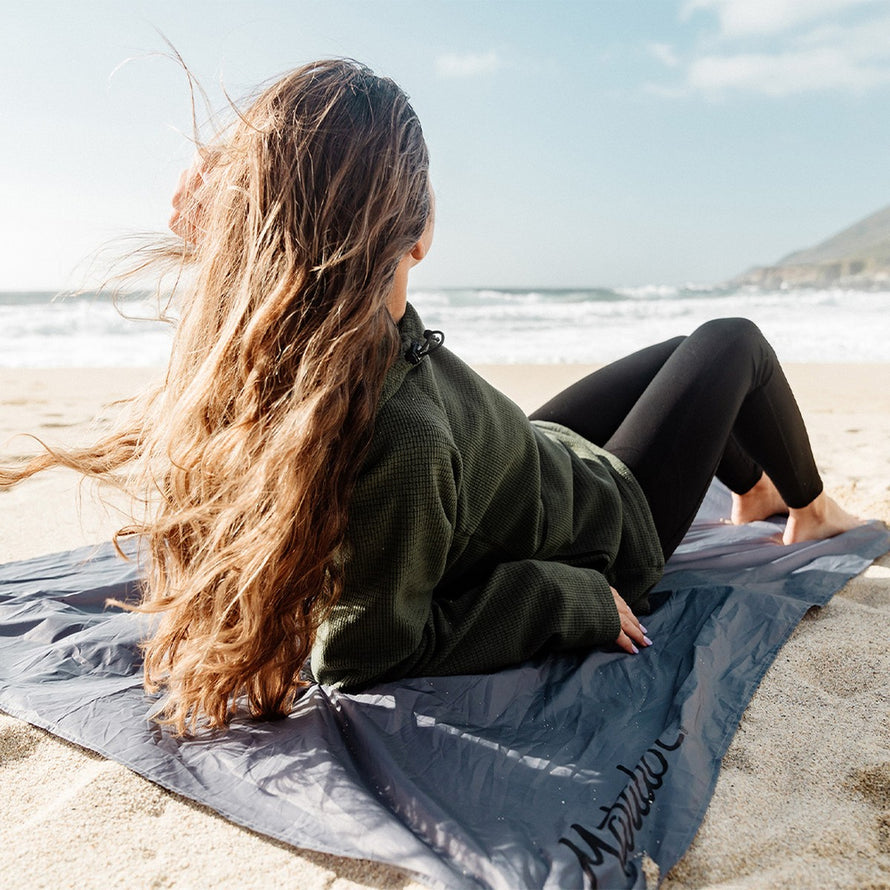 Femme allongée sur la couverture Matador Pocket Blanket au bord de la mer pour confort outdoor