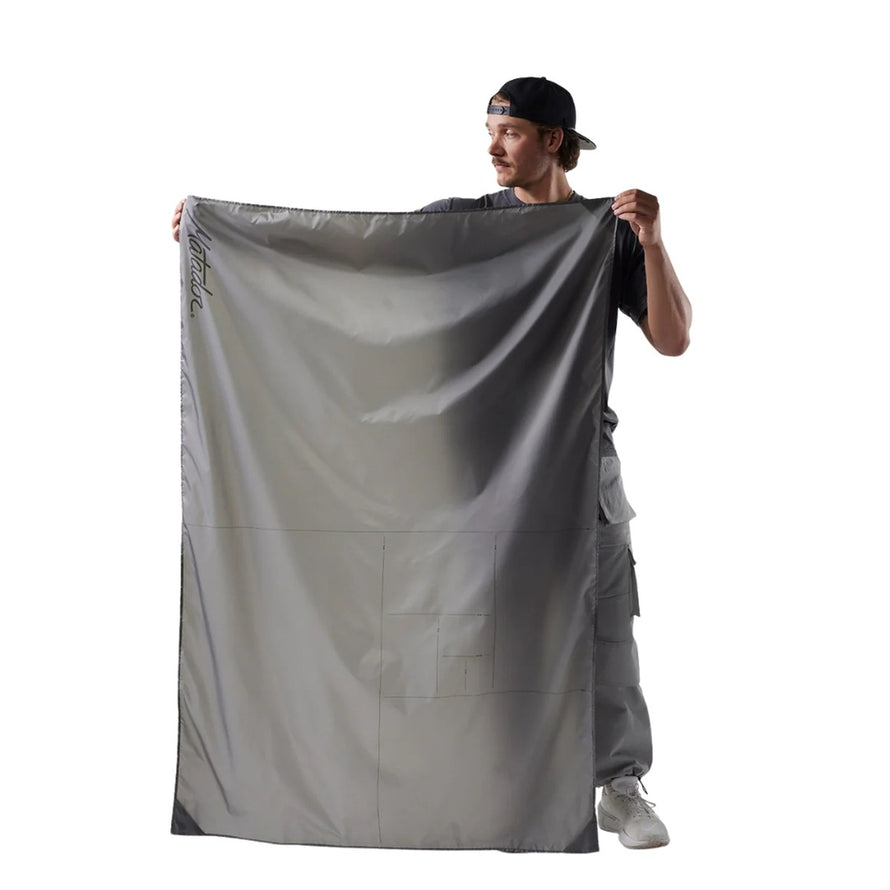 Homme tenant la couverture de poche Matador Pocket Blanket dépliée, idéale pour activités outdoor et protection au sol