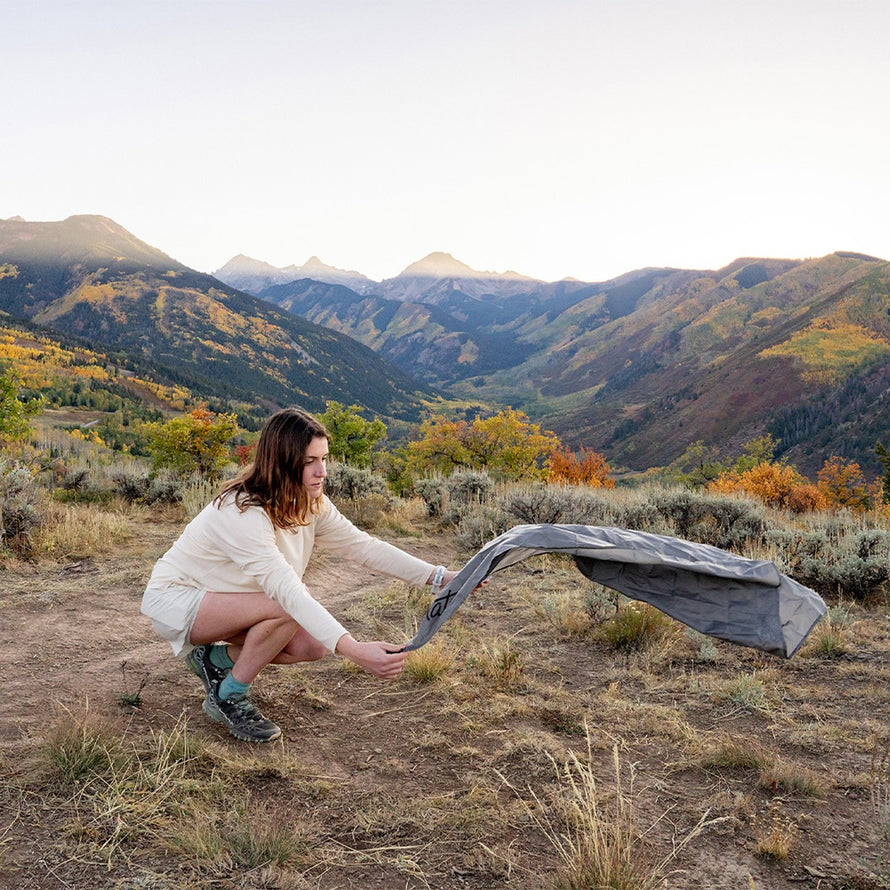 Femme dépliant la mini couverture Matador Pocket Blanket Mini en pleine nature pour activités vélo outdoor