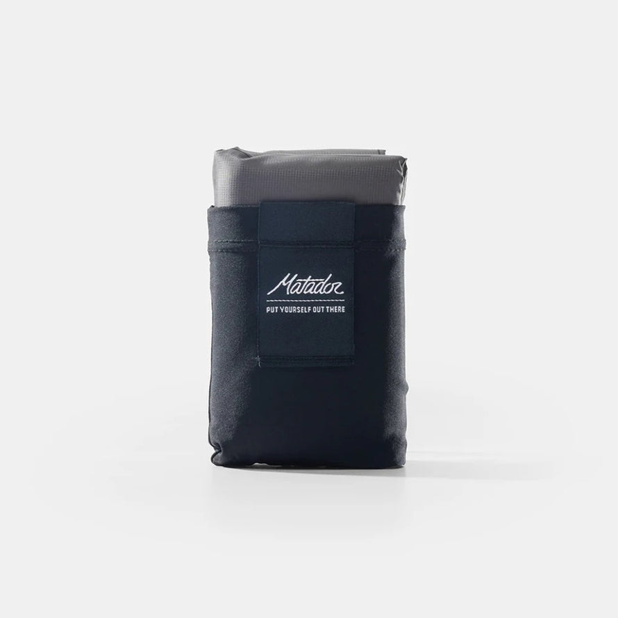 Pochette compacte noire Matador Pocket Blanket avec logo, idéale pour transport facile et activités outdoor