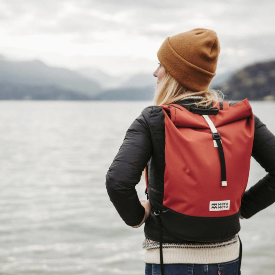 Sac a dos imperméable roll-top MeroMero Wanaka rouge et noir porté en extérieur par une femme