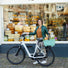 Une femme souriante se tient à côté de son vélo équipé du panier arrière Clipper de chez Newlooks. 