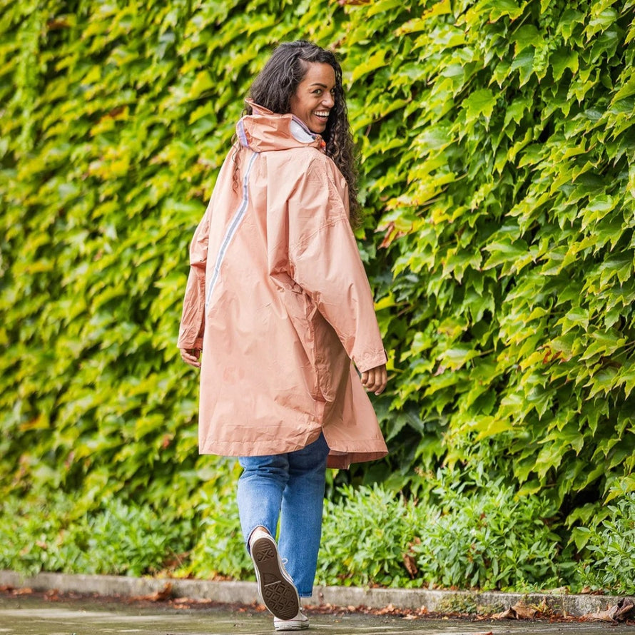 Femme souriante portant poncho de pluie vélo recyclé Le Temps des Grenouilles en extérieur sur fond de feuillage