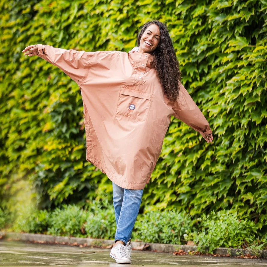 Femme joyeuse en poncho de pluie vélo recyclé Le Temps des Grenouilles couleur rose poudré en extérieur