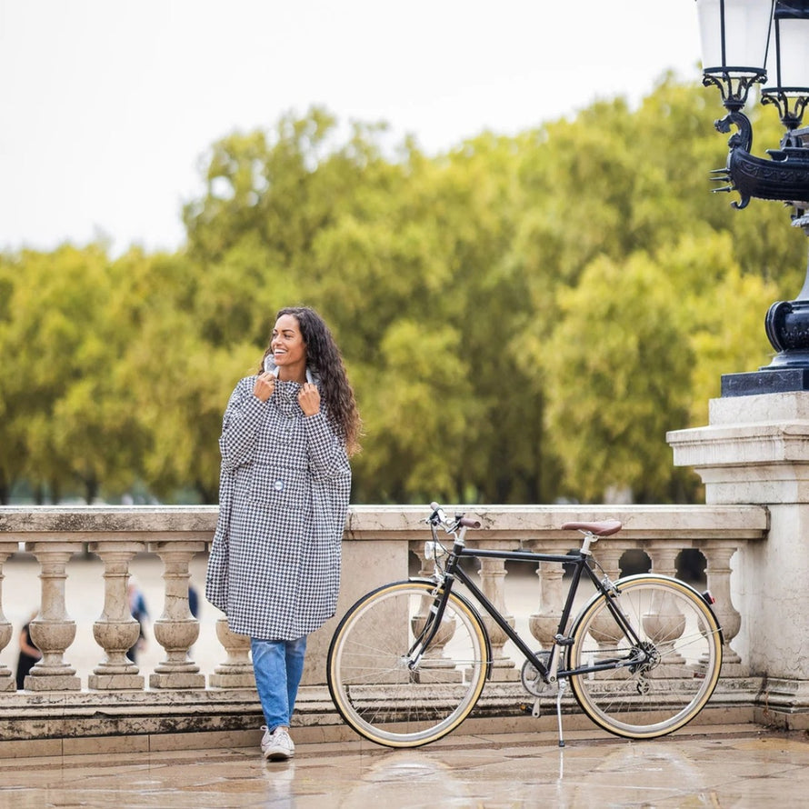 Poncho de pluie vélo recyclé Le Temps des Grenouilles porté par une femme près d'un vélo noir en extérieur