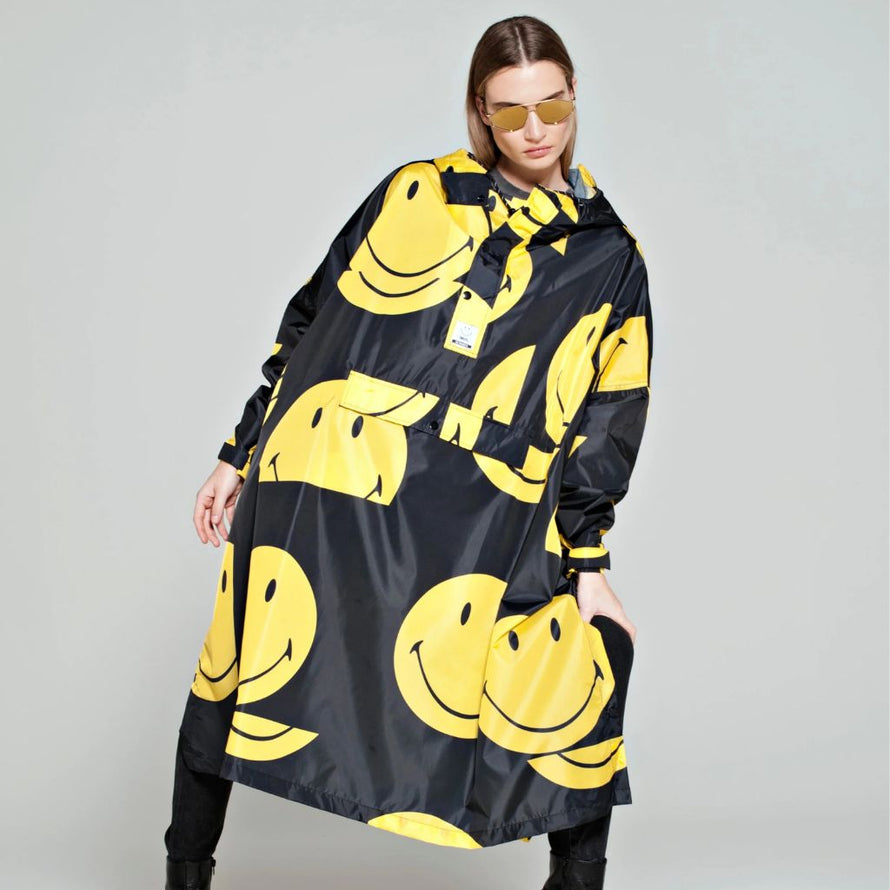 Poncho de pluie Rainkiss All Smiles, imprimé Smiley jaune sur fond noir, look joyeux et urbain pour affronter la pluie avec bonne humeur.