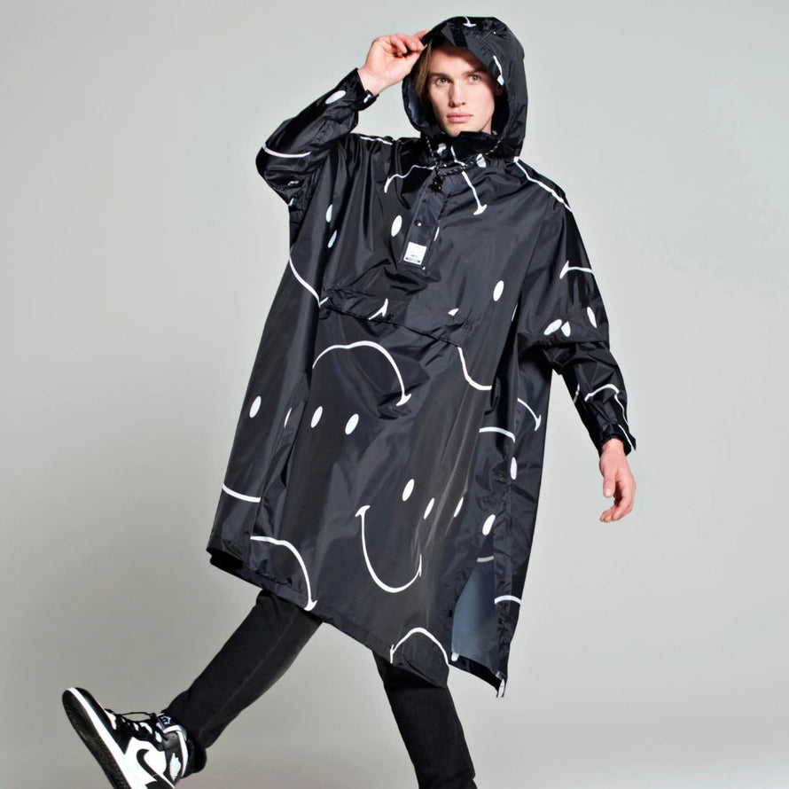 Poncho de pluie Rainkiss Half Moon Smiley, motif graphique noir et blanc orné de demi-lunes souriantes, design audacieux et unisexe pour les jours de pluie.