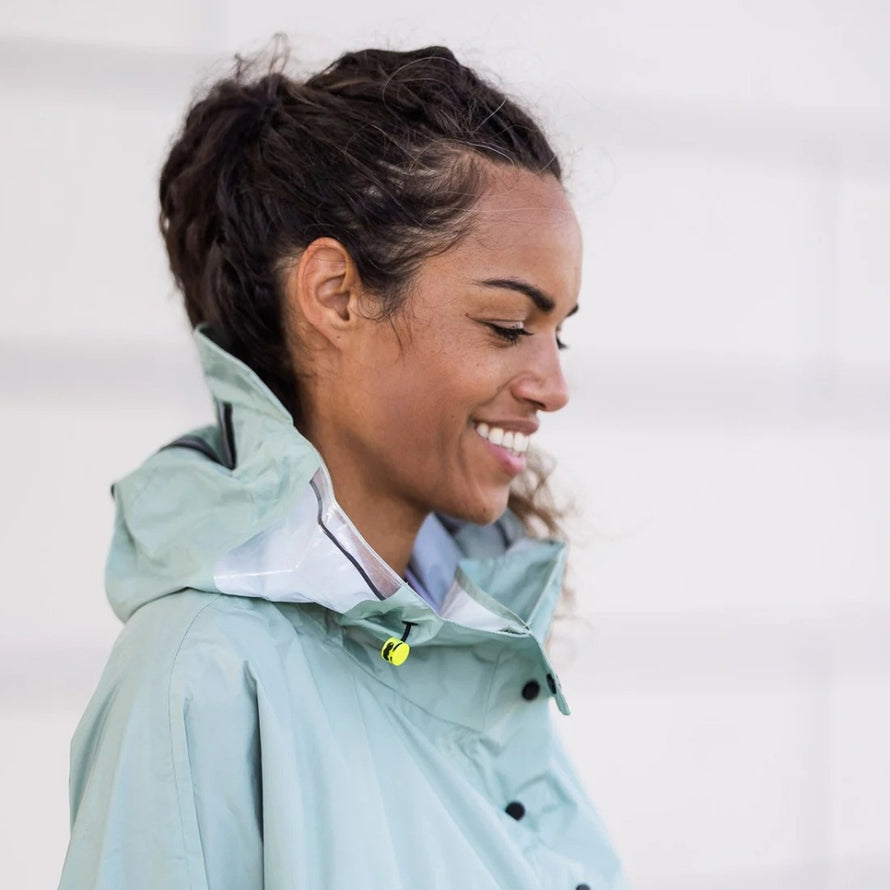 Profil d'une femme souriante en poncho de pluie vélo recyclé Le Temps des Grenouilles avec capuche verte