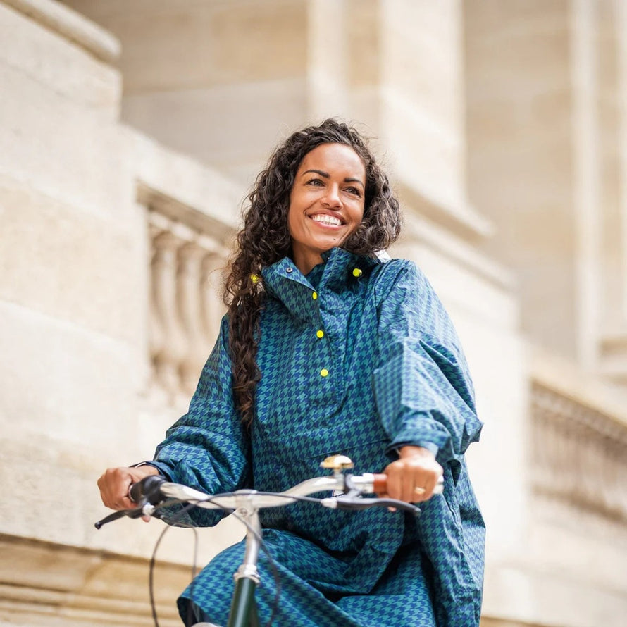 Femme souriante en poncho de pluie vélo recyclé Le Temps des Grenouilles motif pied-de-poule bleu urbain