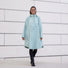 Poncho de pluie vélo recyclé Le Temps des Grenouilles en vert pâle porté par une femme souriante