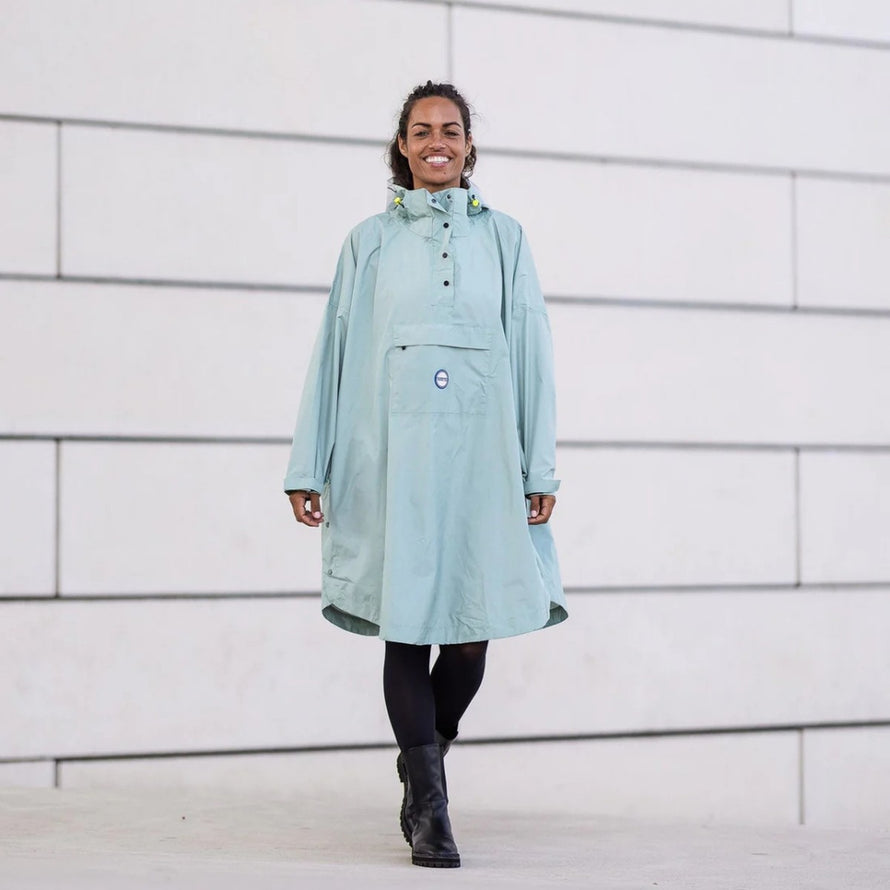 Poncho de pluie vélo recyclé Le Temps des Grenouilles en vert pâle porté par une femme souriante