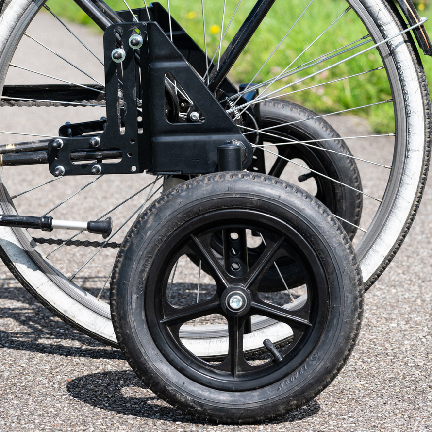 Détail du montage d’une roue stabilisatrice sur un vélo adulte, montrant la fixation latérale sur le cadre et la roue arrière.