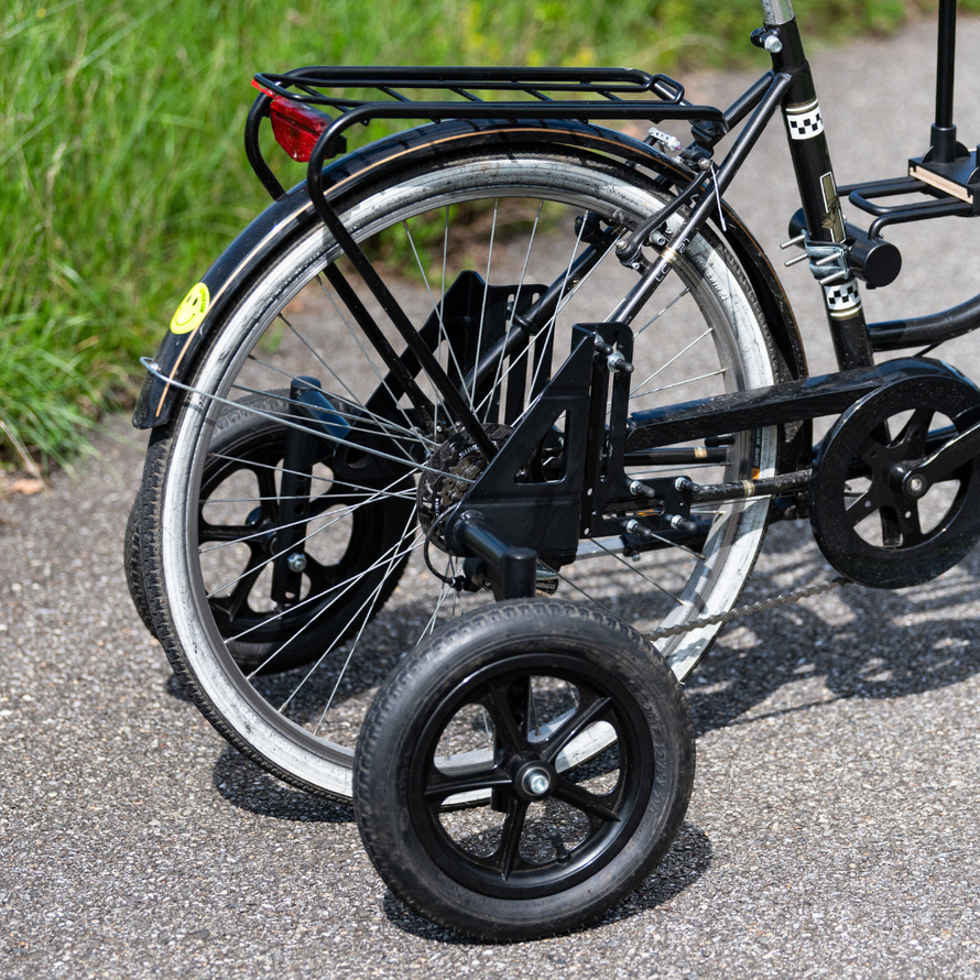 Vue de profil d’un vélo adulte équipé de roues stabilisatrices arrière, fixées de part et d’autre de la roue principale.