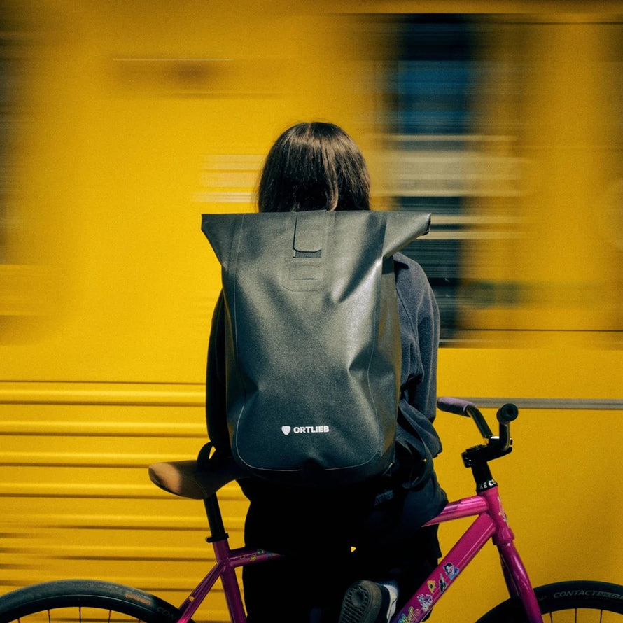 Sac a dos Ortlieb Velocity TIDURA strong 23L noir porté en ville avec velo rose et fond jaune