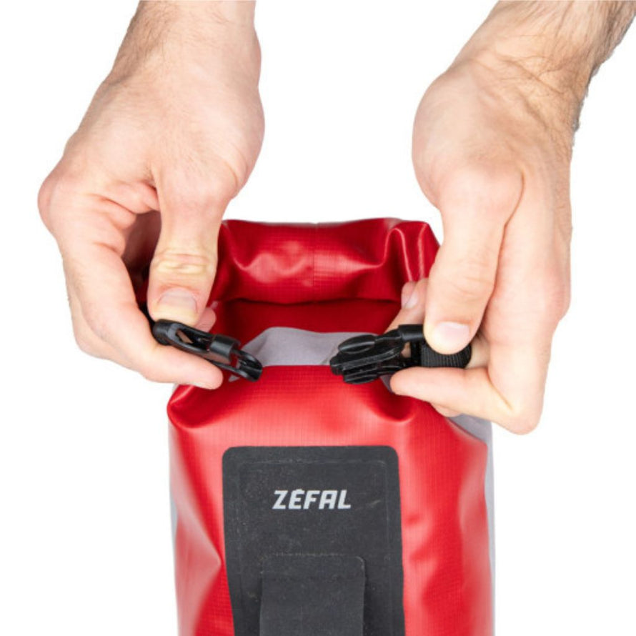 Deux mains attachent la boucle du sac Zéfal rouge pour le fermer