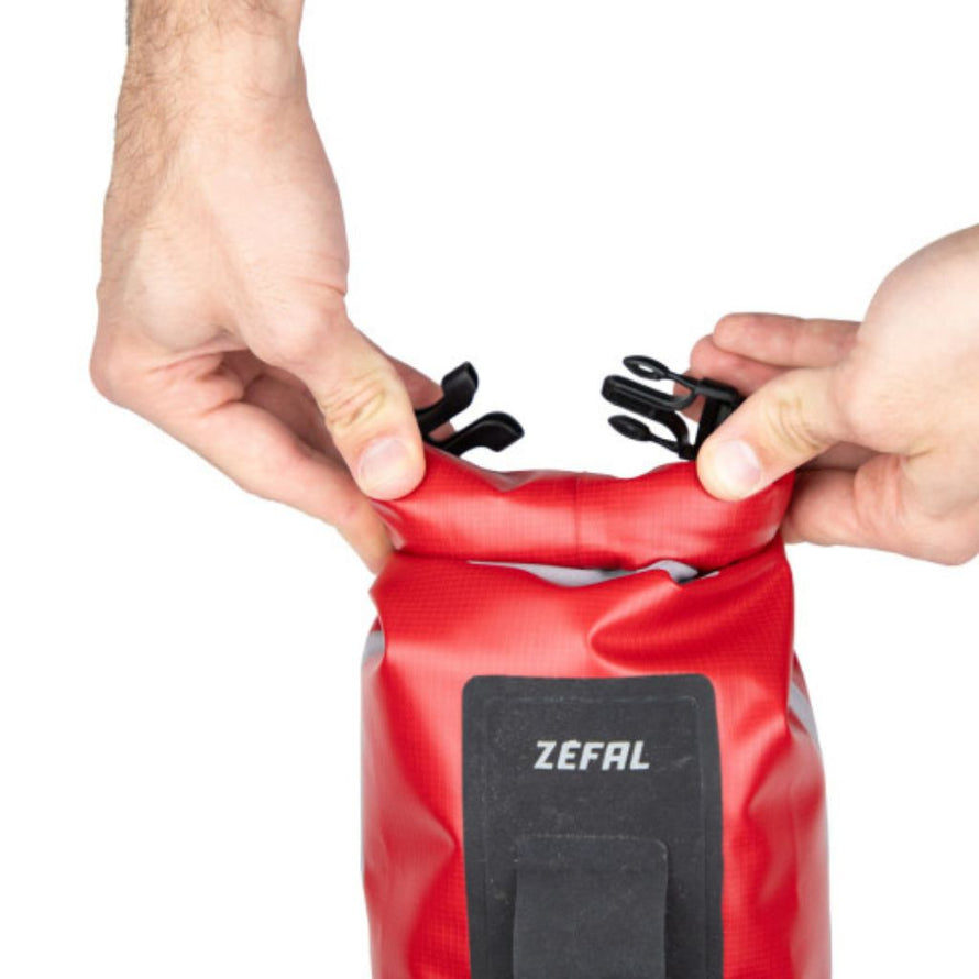 Fermeture du sac Zéfal rouge illustrée avec deux mains en train de rouler la partie supérieure