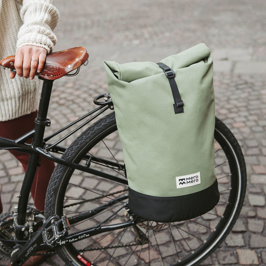 Sacoche vélo MeroMero Annecy verte fixée sur un porte-bagages, utilisée par une cycliste en ville.