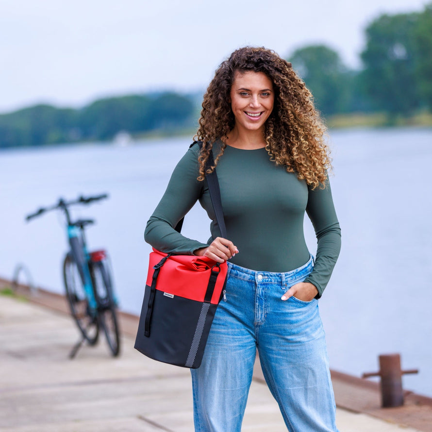 Une jeune femme porte une sacoche vélo rouge et noire Nyborg Newlooxs en bandoulière. 