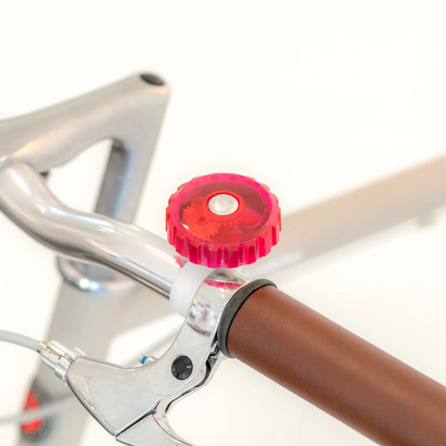 Sonnette vélo rose avec mécanisme intérieur visible Rainette