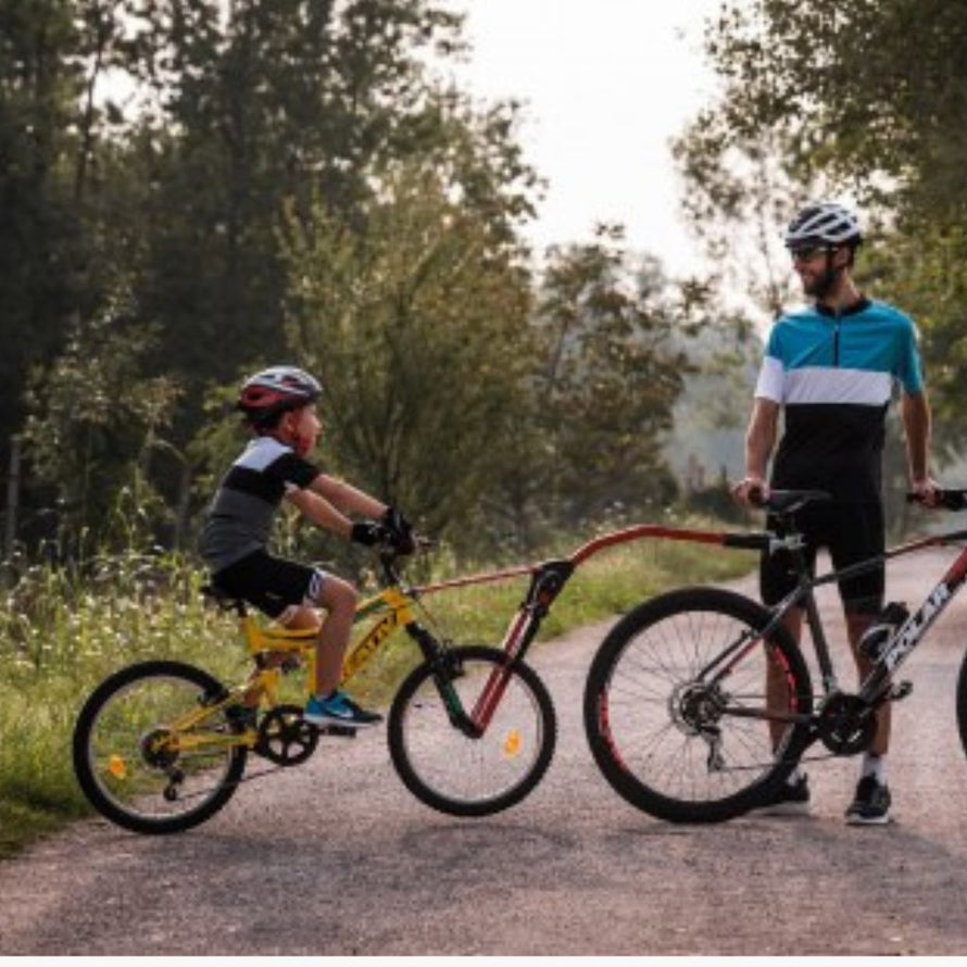 Vue latérale d’un adulte à vélo tirant un enfant avec la barre de traction Trail Angel