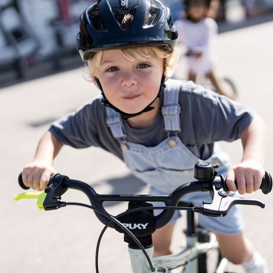 Enfant portant un casque noir utilisant le vélo PUKY LS-PRO 14, avec leviers de frein colorés pour plus de sécurité