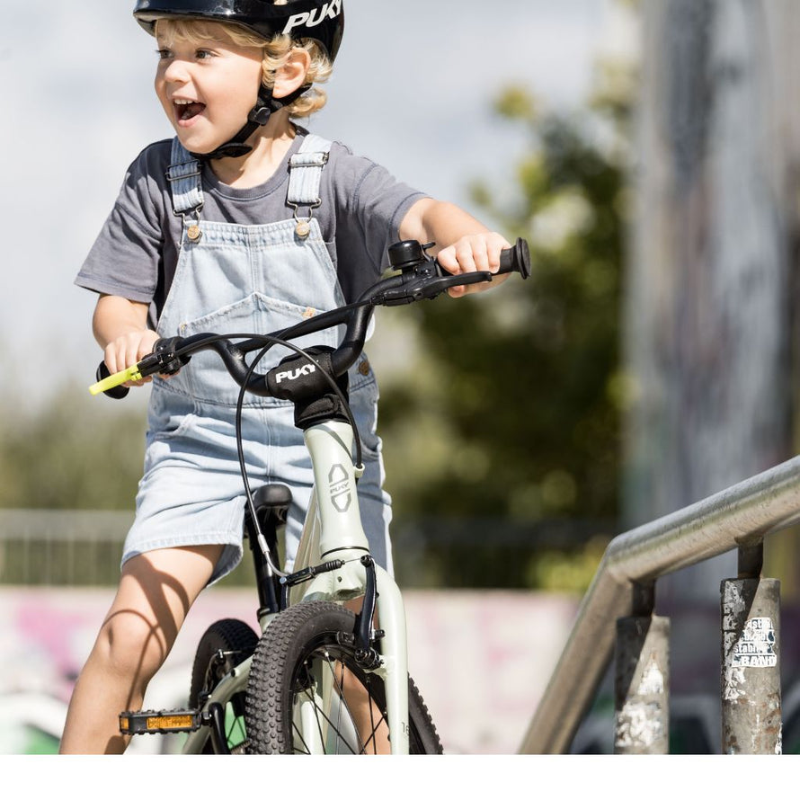 Jeune enfant en salopette roulant avec le vélo PUKY LS-PRO 16 vert, freins colorés et position confortable pour apprendre à pédaler