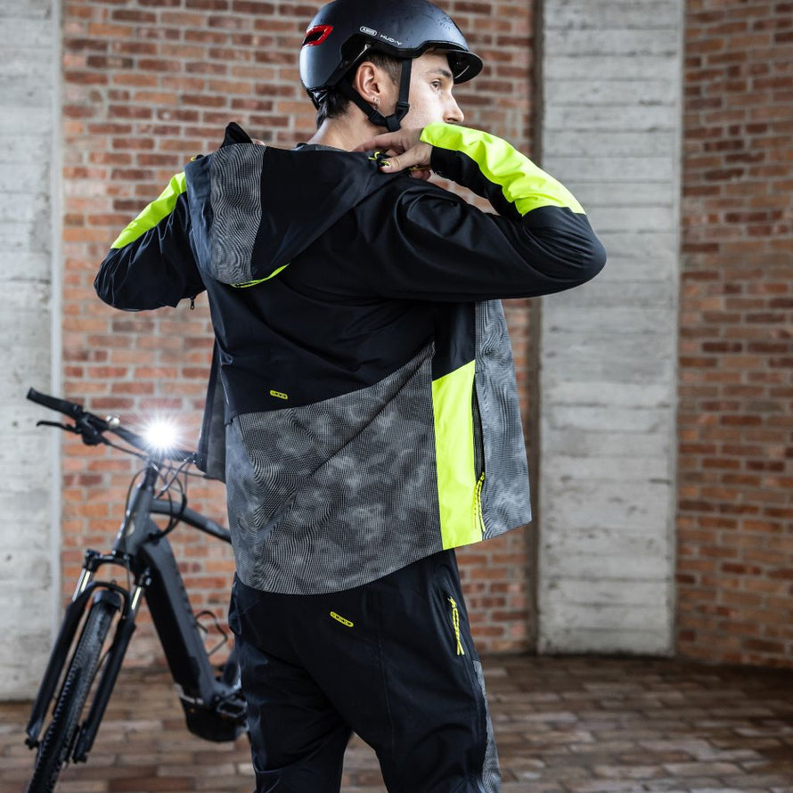 Cycliste ajustant la capuche de sa veste vélo Wowow Etna, un vêtement technique étanche et respirant à haute visibilité.