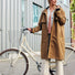 Femme tenant son vélo habillée de la veste imperméable Imbris couleur camel, coupe trench élégante et fonctionnelle.