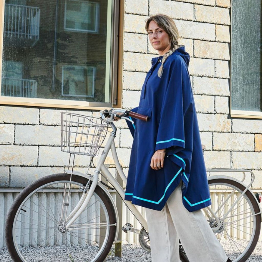 Femme portant un poncho bleu Imbris Weathergoods Sweden, debout avec son vélo urbain, prête pour ses trajets quotidiens.