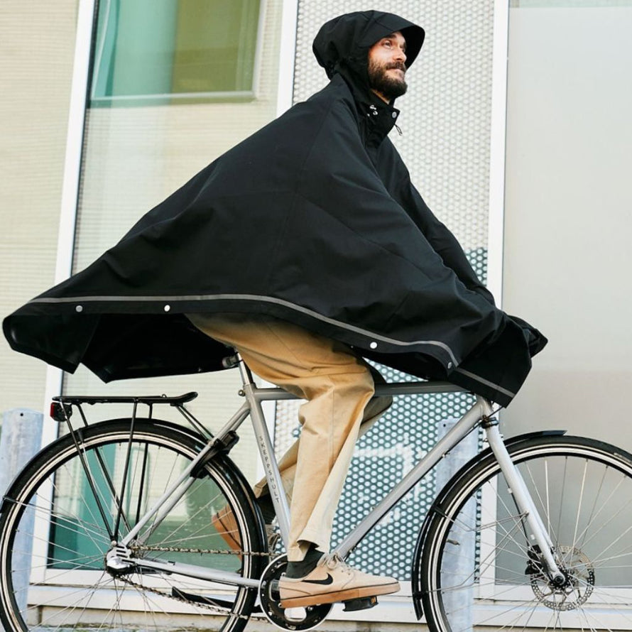 Homme roulant à vélo avec le poncho noir Imbris Weathergoods Sweden, protection imperméable et coupe-vent.