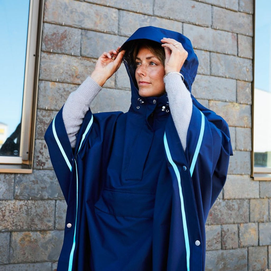 Femme ajustant la capuche de son poncho de pluie bleu Imbris Weathergoods Sweden, élégant et imperméable.