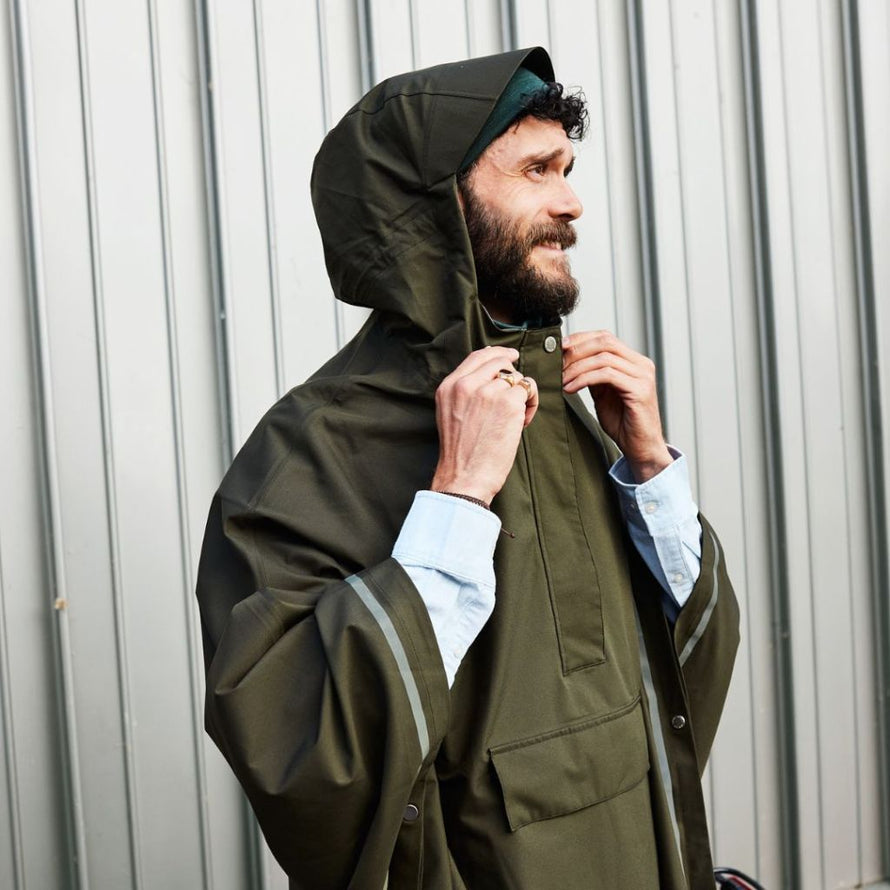 Gros plan d’un homme fermant la capuche de son poncho vert Imbris Weathergoods Sweden, détails raffinés et fonctionnels.