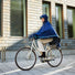 Femme à vélo portant le poncho bleu Imbris Weathergoods Sweden, capuche ajustée et bande réfléchissante ton sur ton.