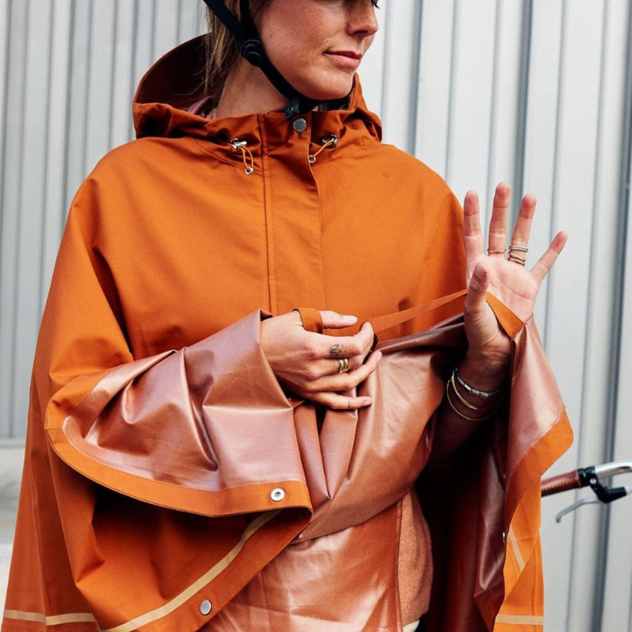 Gros plan d’une femme avec le poncho cuivre Imbris Weathergoods Sweden, tenant la sangle de maintien pour protéger ses mains.